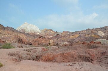 barren landscape with some low plants and beautiful colored mountains in background at Hormuz island, Iran