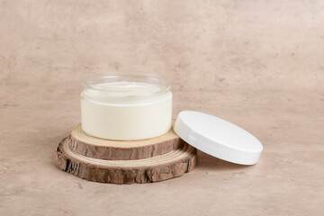 Cosmetic cream or moustirizer mockup on wooden podium over pastel beige background. Open round glass jar with aesthetic swirls face cream, copy space, design element