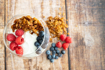 granola with raspberries and blueberries with yogurt in a wine glass on a wooden background