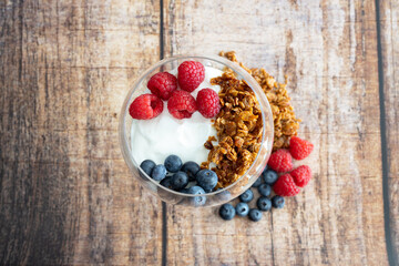 granola with raspberries and blueberries with yogurt in a wine glass on a wooden background