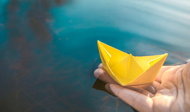 Yellow lonely floating paper boat in hand. Colorful sailing ship in big blue spring puddle, river water.Warm wet rainy weather.Hello spring,autumn.Children play,have street fun outdoors.Way to future
