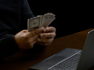 Computer and hands of a man wearing a black shirt, sitting on a chair and a table, is a thief,...