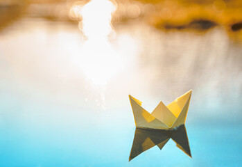 Yellow floating paper boat. Colorful sailing ship in big blue spring puddle, river water on winter street. Warm wet rainy weather, old grass. Hello spring, autumn. Children play, have fun outdoors