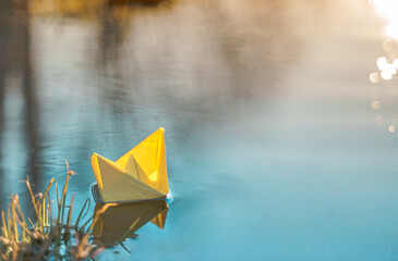 Yellow floating paper boat. Colorful sailing ship in big blue spring puddle, river water on winter street. Warm wet rainy weather, old grass. Hello spring, autumn. Children play, have fun outdoors