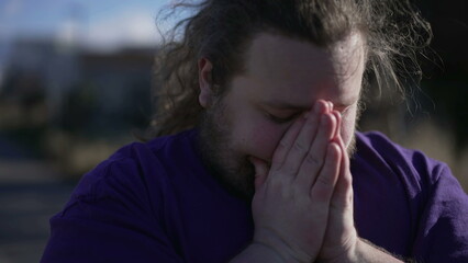 One young man praying to God during hard times. Faithful person in prayer outdoors clenched hands together seeking help