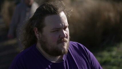 One worried overweight man standing outside with preoccupied expression. A thoughtful fat guy close up face with anxious emotion. Tracking shot