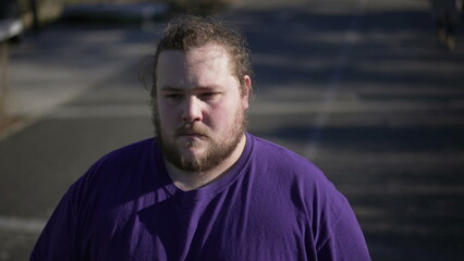 One worried overweight man standing outside with preoccupied expression. A thoughtful fat guy close up face with anxious emotion. Tracking shot