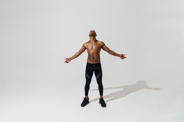 Attractive sporty man with muscled naked body on white studio background looks up with open arms
