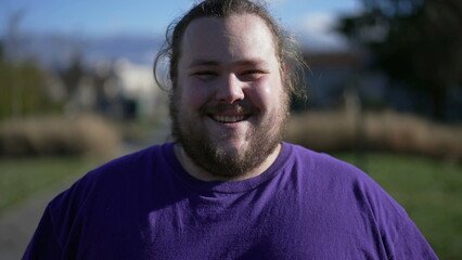 One happy overweight man walking forward outdoors smiling. A joyful fat guy portrait face close up in tracking shot