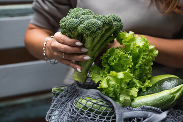 Female hands with a string bag and green vegetables close-up. A girl buying food. The concept of healthy nutrition, vegetarianism and ecology. Refusal of plastic bags.