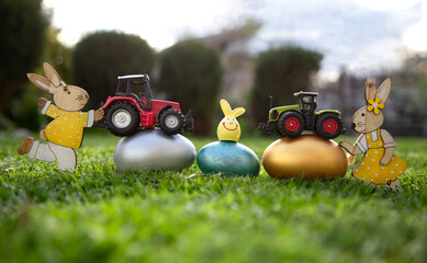 two models of toy tractors stand on painted multi-colored eggs that lie on the grass. concept of commercial easter greetings for farms, agribusiness. postcard. copy space