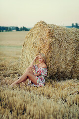 Naklejka na ściany i meble Young beautiful woman sits with closed eyes on haystack . Countryside holiday