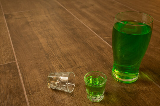 shot glasses lined up on wooden bar background filled with green spirit cocktail and shamrock, drunk at celebration for St Patrick's day 2023. Irish holiday popular drinking event when people party
