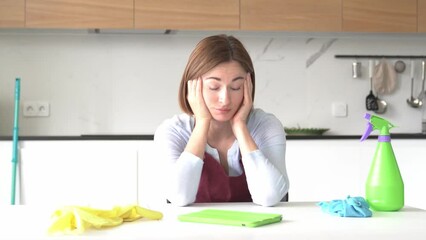 Tired attractive woman in yellow rubber gloves and red apron sits and wipes the table and feeling bad after exhausting cleaning day. Household concept