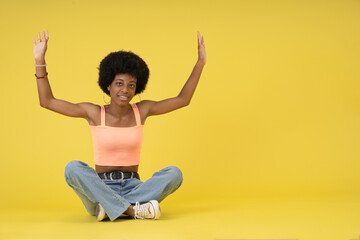 Young black lady with afro hairstyle, seated on the floor raising her arms