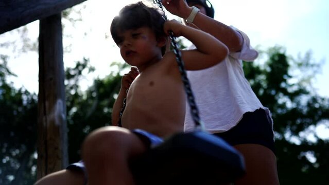 Happy young boy turning in playground swing enjoying summer holiday vacations outside shirtless. Kid playing outside having fun