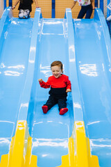 Happy, smiling little boy, preschool child descends, slides down a plastic slide on an indoor...