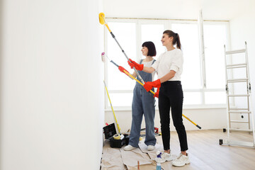 Young attractive women makes repairs in apartment and paint walls in white color using paint...