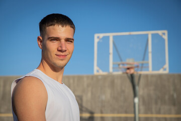 A smiling basketball player on a basketball court with a hoop behind him