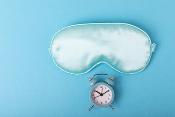 Sleep mask and alarm clock on a blue background. The concept of rest, sleep quality, good night,...