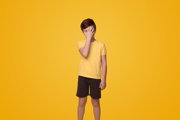 Fototapeta na wymiar Young caucasian boy put hand on face, facepalm epic fail isolated on yellow background studio portrait. People lifestyle concept