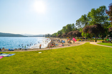 Fototapeta na wymiar Tourists and local Idahoans enjoy a summer afternoon at the City Beach and Park along Lake Coeur d'Alene, in the Inland Northwest of the US. 