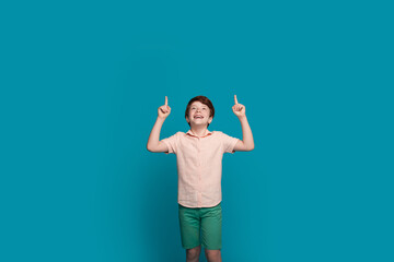 Smiling little boy pointing up at copy space above his head, recommending something, isolated on...