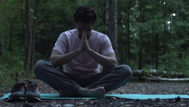 Young handsome man doing yoga in lotus position in the wood. Training and sport on nature concept	