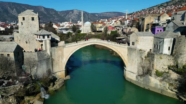Aerial drone view of the Old Bridge in Mostar city in Bosnia and Herzegovina during sunny day. Blue turquoise colors of Neretva river. Unesco World Heritage Site. People walking over the bridge.