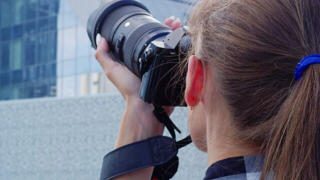 Young woman takes pictures while standing next to modern building. Photographer traveler takes pictures of city sights. Back view