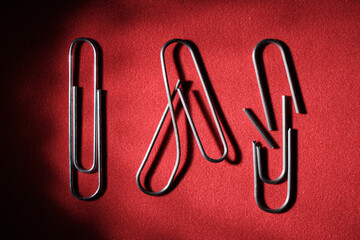 Three paper clips on a red background, whole, bent and broken. The concept of breaking the bonds