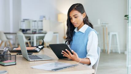 Trendy marketing professional using an online app to network, meet deadlines and stay connected during office hours. Young business woman using her laptop and tablet while working in the office.