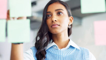 Focused young business woman thinking while brainstorming solutions for a project and marketing strategy in a creative startup agency. Designer planning ideas and information on a window in an office