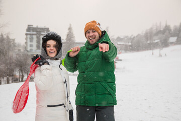 Beautiful  couple in love spending time outdoor on a snowy winter day, holding sledge red and green.