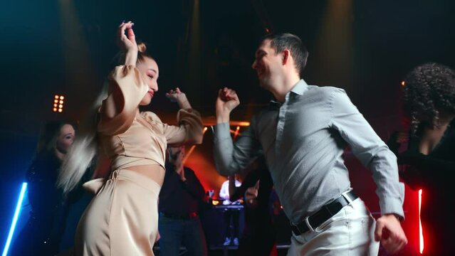 Smiling elegant fashion woman dancing with charismatic man flirting at nightclub illuminated party