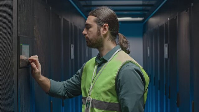 Confident male IT specialist walking along row if operational server racks, checking work of supercomputers