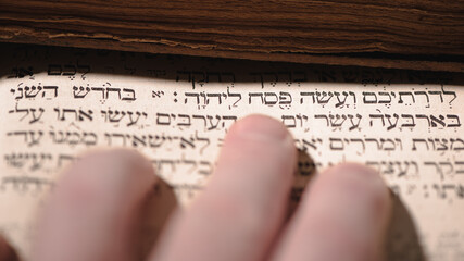 Fingers on page of old book Torah. Selective focus on snippet Hebrew Bible text that translates in english: offer the Passover sacrifice to Jehovah. Closeup.