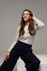 Stylish young girl with long hair and glowing skin posing on gray background.