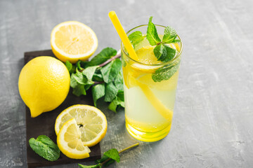 Lemonade drink or mojito cocktail in a glass with straw, lemon fruit and mint leaves, refreshing summer beverage