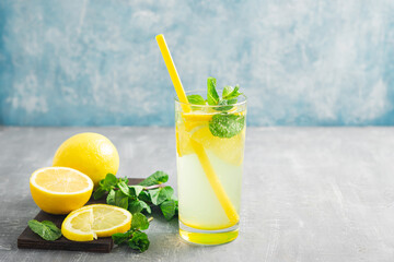 Lemonade drink or mojito cocktail in a glass with straw, lemon fruit and mint leaves, refreshing summer beverage