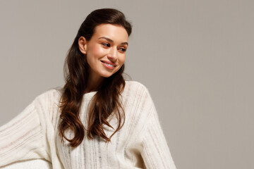 Happy young woman sitting on sofa at home and looking at camera. Portrait of comfortable woman in winter clothes relaxing on armchair. Portrait of beautiful girl smiling and relaxing during autumn.