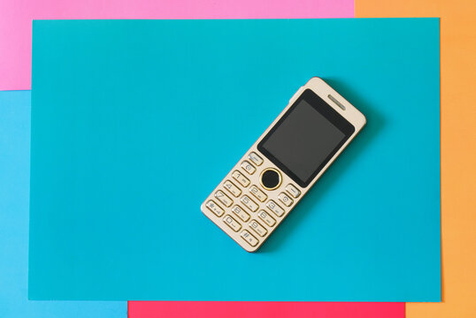 A small push-button mobile phone on a colored background.