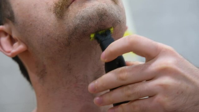 The man shaves his big beard. The guy shaves off his big beard. Young guy shaves his beard at home. Personal care