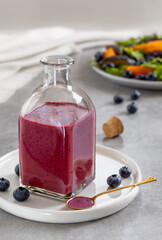 Salad dressing or Blueberry sauce with fresh blueberries, oil, balsamic vinegar, honey, salt and pepper served in glass bottle. Ingredients and plate with salad on background. Vertical.