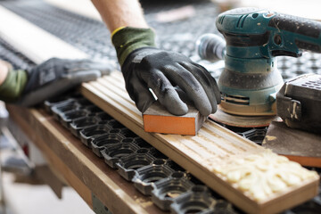 Hands of a carpenter manually sanding the edge of a wooden block with sandpaper on a hand tool in a woodworking or carpentry workshop