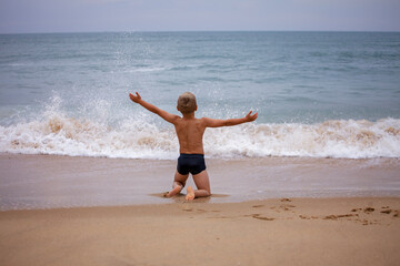Fototapeta na wymiar A boy of 7-8 years old sits on the ocean shore with his arms open towards the wind and waves. Storm on the ocean in summer. The concept of freedom, courage and challenge. Place for text