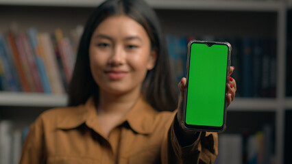 Close-up smiling korean woman businesswoman holding phone showing green screen smartphone touchscreen touch display mockup with chroma key advertise mobile application promote digital device cellphone
