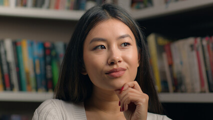 Portrait pensive korean woman standing in library near bookshelf think ponder deep in thought in search solution happy female comes up with good idea remembers make gesture raises finger finds answer