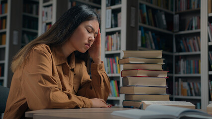 Tired unwell young korean woman student preparing for exam in university library feeling headache suffering from study overload having painful feel exhausted suffer from chronic migraine overworking