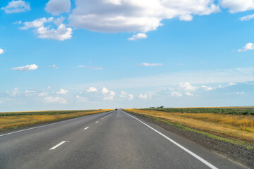 Marking lane on gray asphalt on empty highway road among endless steppe under blue sky with clouds